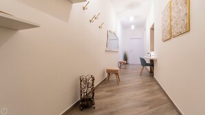 A hallway with a wooden floor, a small bench, a decorative metal stand, and a desk with a chair. - Baracca 7 B - One Bedroom Apartment, Sleeps 4 (Bologna)