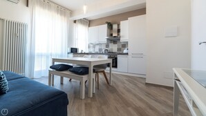 A modern kitchen with white cabinets, a dining table with two chairs, and a blue sofa with cushions. - Baracca 7 B - One Bedroom Apartment, Sleeps 4 (Bologna)