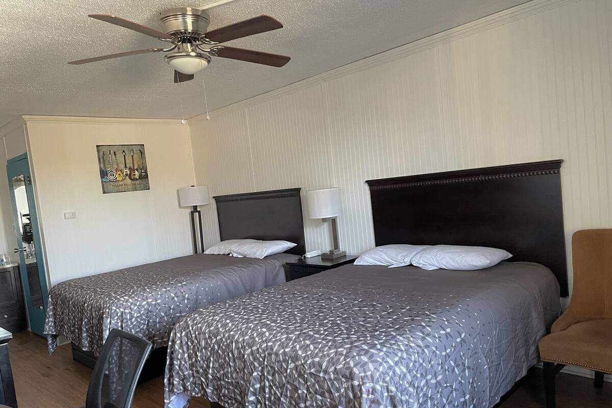 Une chambre d’hôtel avec deux lits, un ventilateur de plafond, un bureau avec une chaise et un tableau au mur.