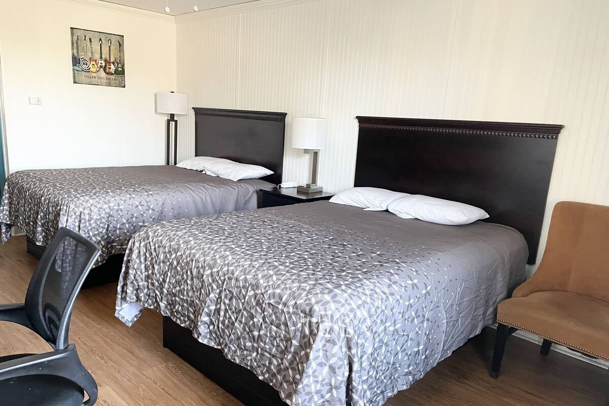 Une chambre d’hôtel avec deux lits, une chaise, un bureau et une lampe.