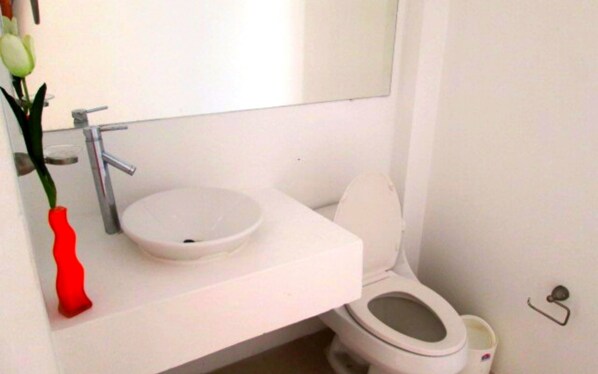 Une petite salle de bain avec un lavabo blanc, des toilettes et un miroir au-dessus du lavabo.