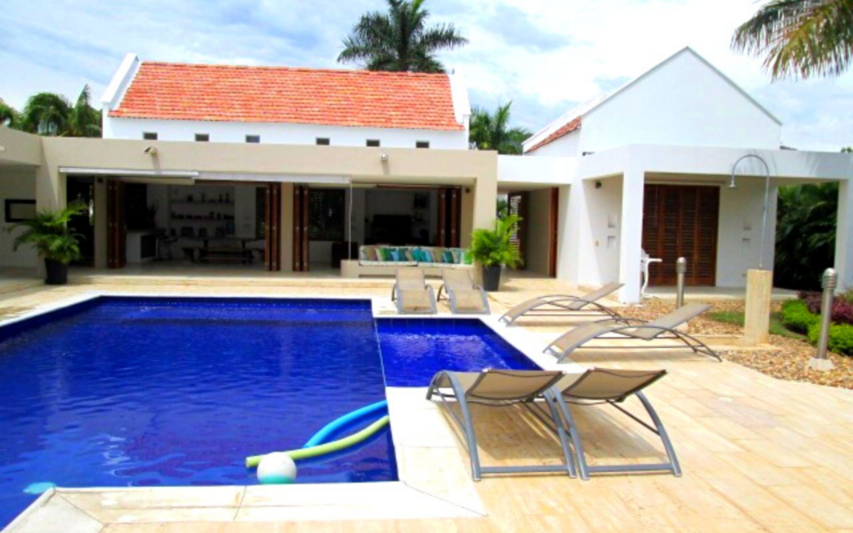 Ein modernes Haus mit Swimmingpool, Liegestühlen und einer überdachten Terrasse.