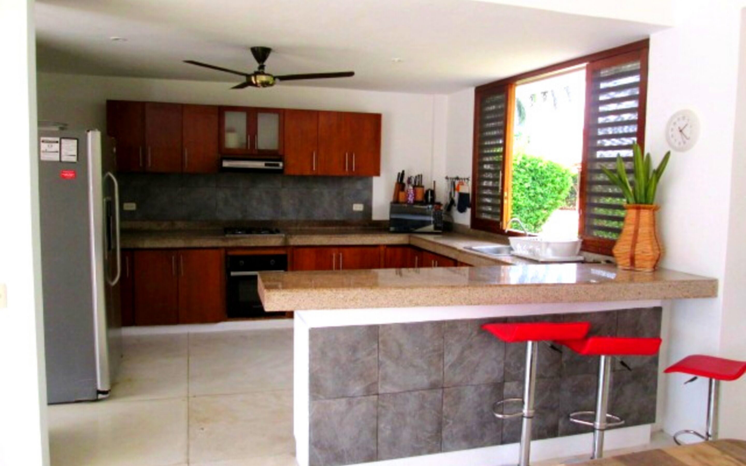 A modern kitchen with wooden cabinets, a built-in stove, and a window with blinds.