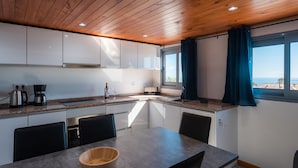 A modern kitchen with a wooden ceiling, white cabinets, a granite countertop, and a dining area with a table and chairs. - Beautiful country Villa with a small house onsite which together sleeps 6 people (Estreito da Calheta Madeira)