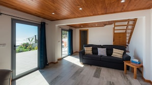 A modern living room with a wooden ceiling, a black sofa with patterned cushions, and a view through a glass door to an outdoor area. - Beautiful country Villa with a small house onsite which together sleeps 6 people (Estreito da Calheta Madeira)