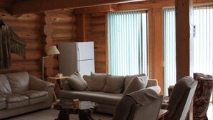 En stuga med träpanel på insidan, inredd med en soffgrupp, en lampa och ett kylskåp.