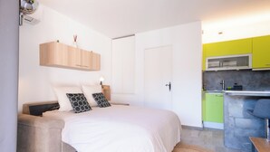 Ein modernes Schlafzimmer mit Bett, Nachttisch und einem kleinen Schreibtisch. Es gibt eine Küchenzeile mit Mikrowelle und Spüle.