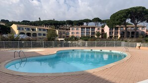 Ein Schwimmbecken mit gefliestem Deck, umgeben von einem weißen Zaun, mit Gebäuden im Hintergrund.