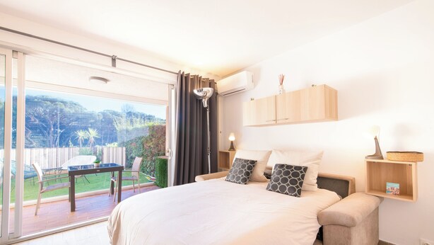 Ein Schlafzimmer mit einem großen Bett, einem Nachttisch, einem Fenster mit Vorhängen und Blick ins Freie.