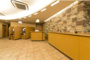 Una zona de recepción con pared de piedra, mostrador y un área de estar con sillas.