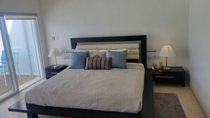 A bedroom with a bed, two bedside tables, two lamps, a window, and a view of the outside.