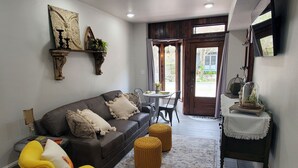 Una sala de estar con sofá, sillón amarillo, otomanas y un comedor con mesa y sillas.