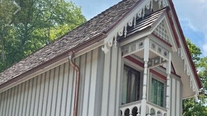 Un edificio de dos pisos con base de piedra, un balcón con barandillas blancas y una sección inferior de ladrillo rojo.