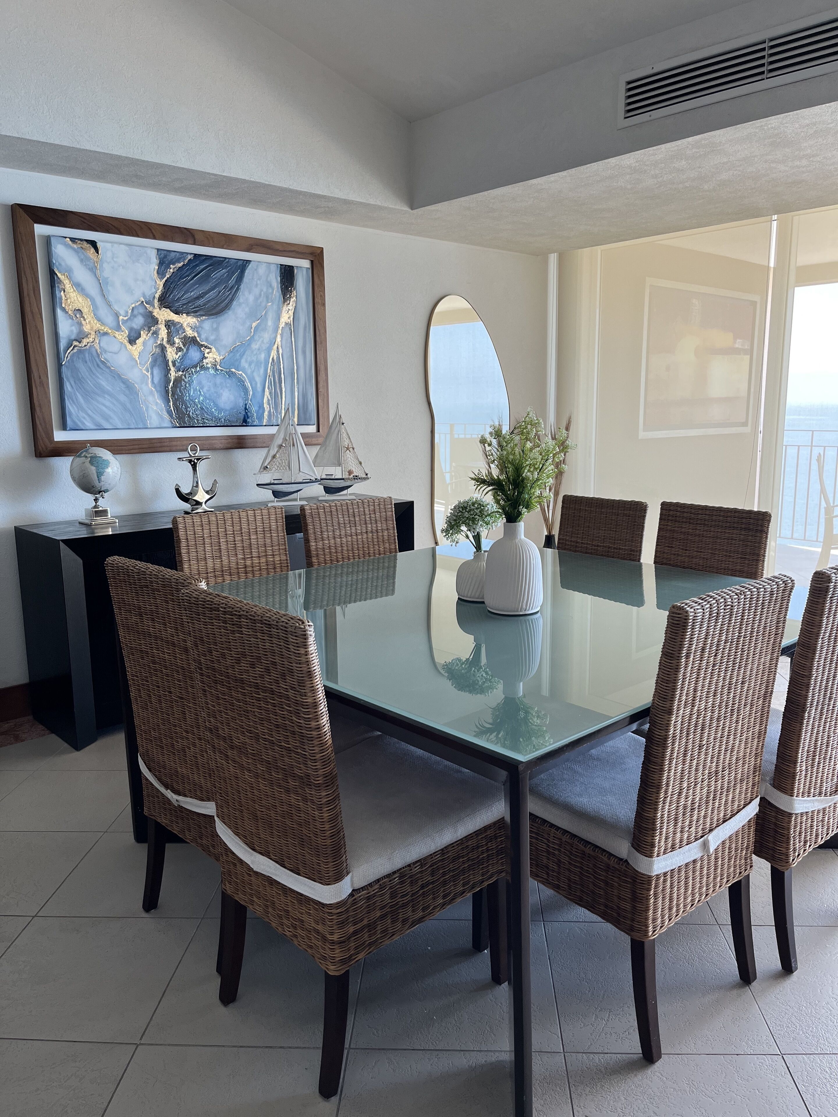 A dining area with a glass table surrounded by wicker chairs, a decorative globe, and a sailboat model on a console table.