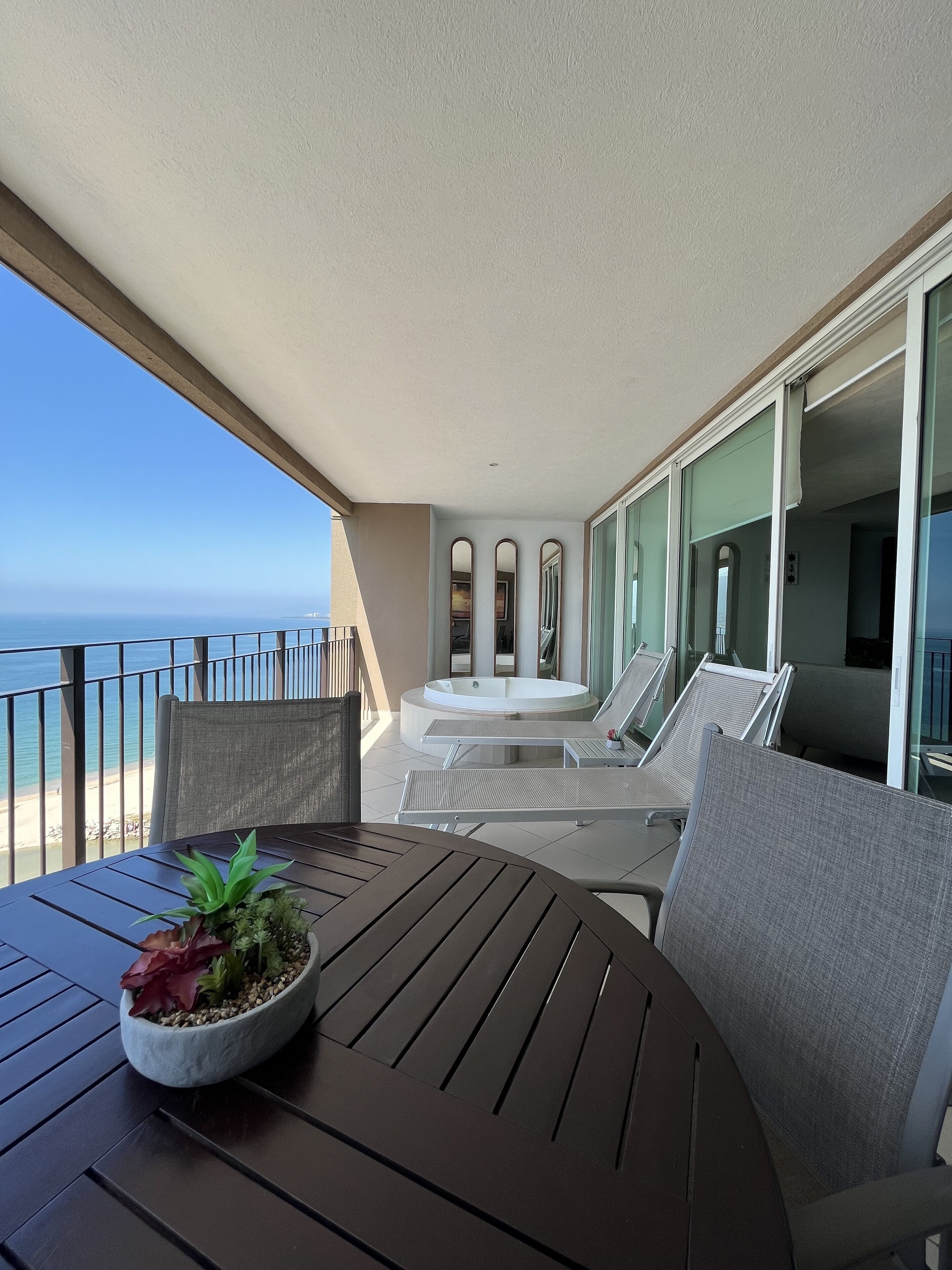 Un balcon avec vue sur l’océan, une table ronde agrémentée d’une plante et des fauteuils de relaxation.