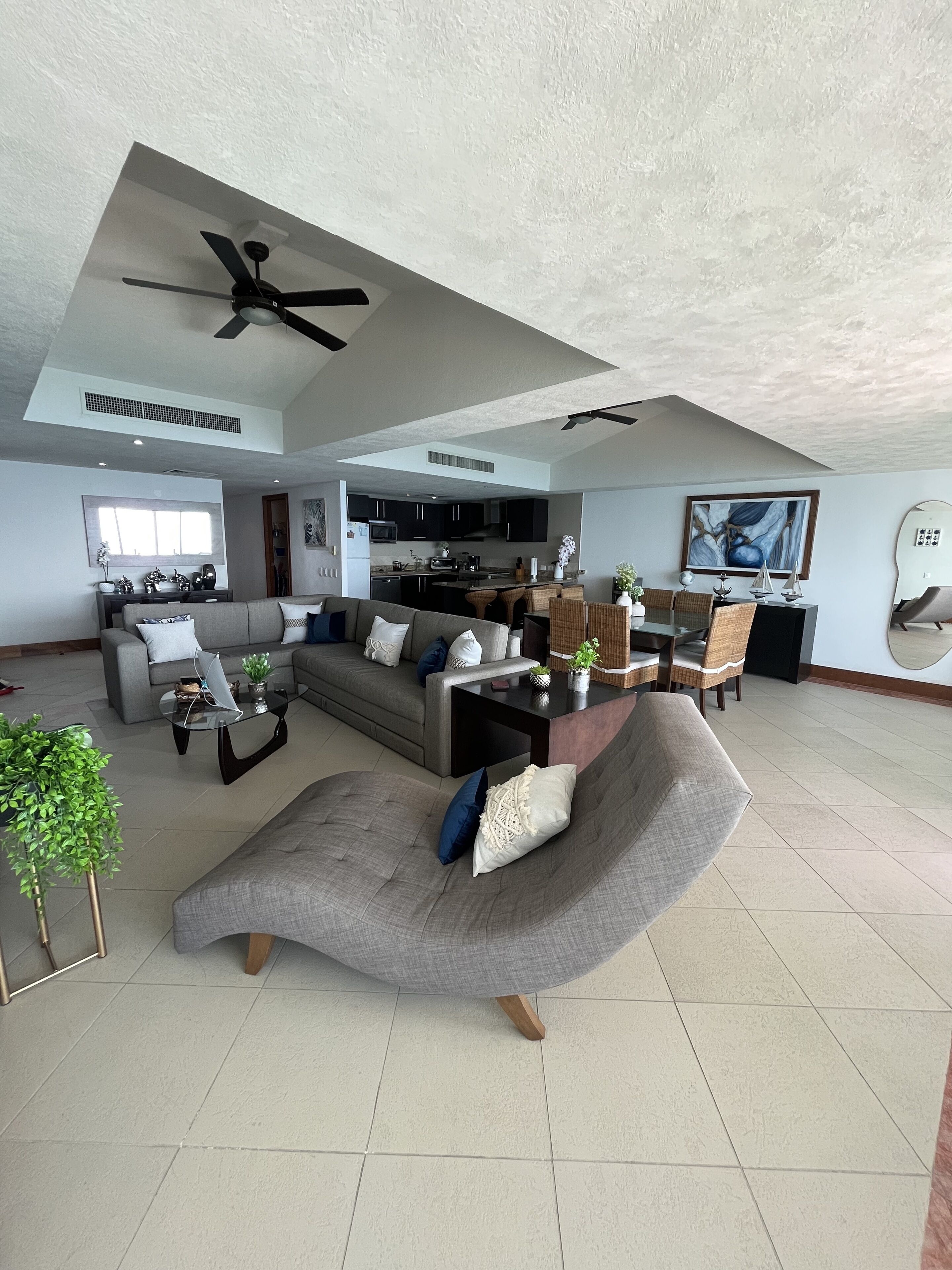A spacious living area with a large gray sectional sofa, a glass coffee table, and a dining area with wicker chairs.