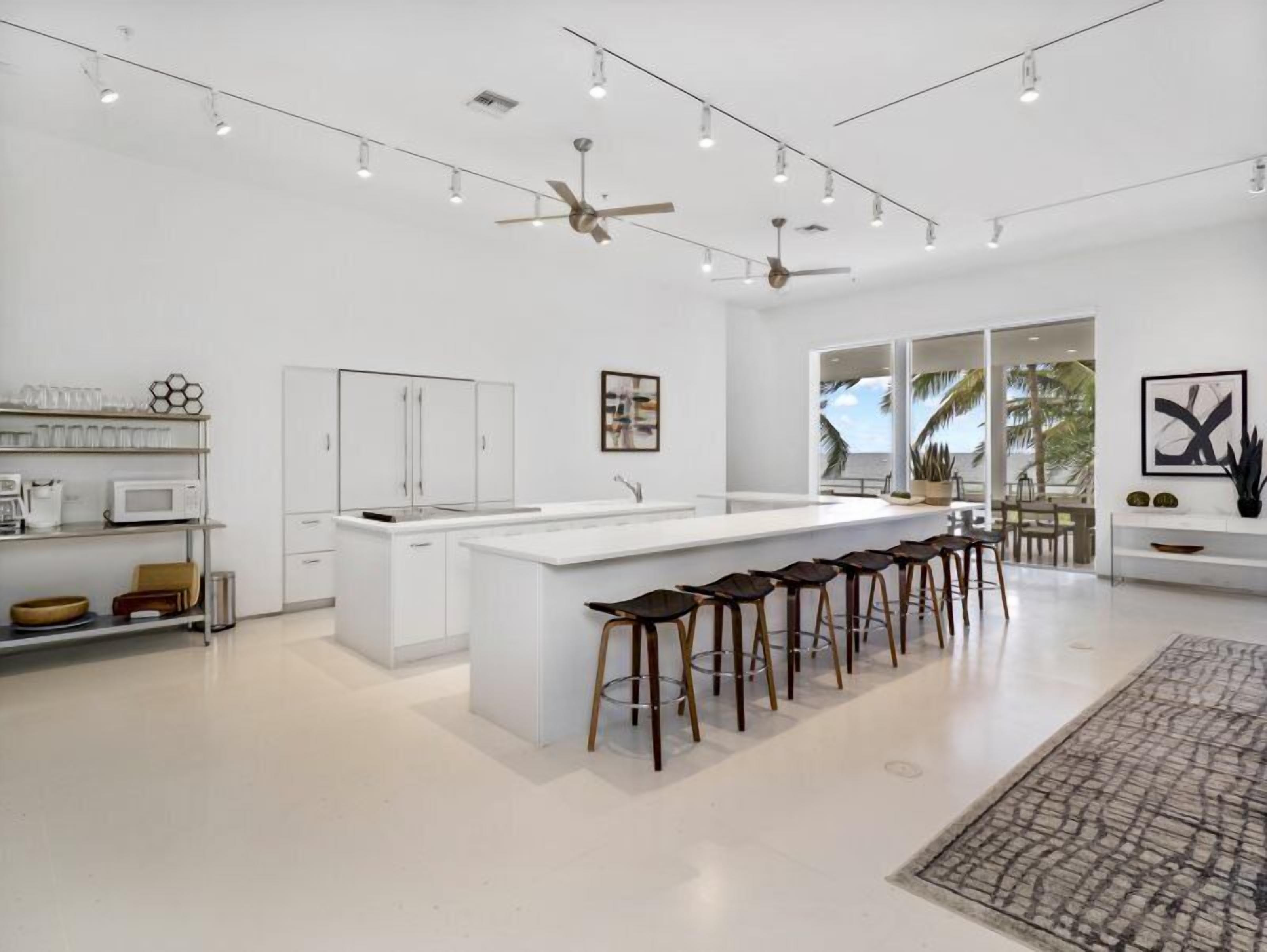 Una cocina moderna con una isla central, taburetes de bar y un amplio ventanal con vistas a palmeras.