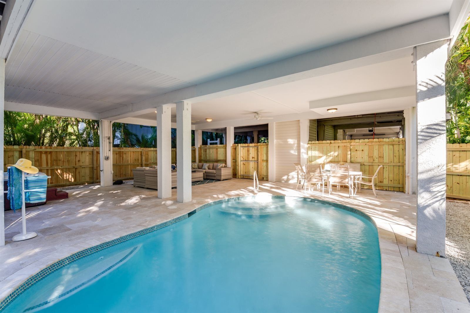 A covered swimming pool area with a built-in seating area and a wooden fence.