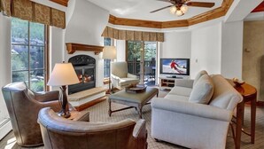 Una sala de estar acogedora con chimenea, asientos cómodos, televisión y ventilador de techo.