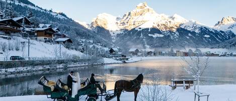 Un lago cubierto de nieve con un carruaje tirado por caballos y una pareja con vestimenta de boda.