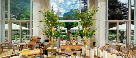 A spacious indoor dining area with large windows, a buffet setup, and a view of a mountainous landscape.