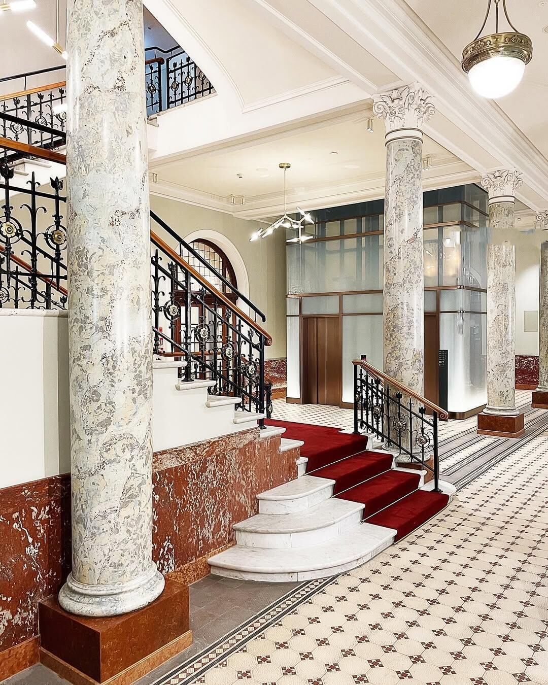 A grand staircase with marble columns and red carpeted steps leading to a second floor.