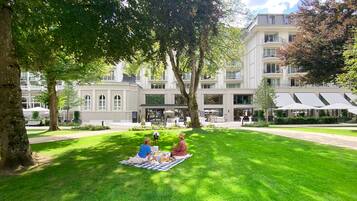 Relax in a serene outdoor setting with tables and umbrellas, surrounded by a well-maintained lawn.