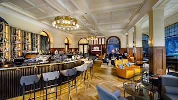 Un amplio bar con una barra alta, diversas opciones de asientos que incluyen taburetes y sofás, y un gran ventanal con vistas al exterior.