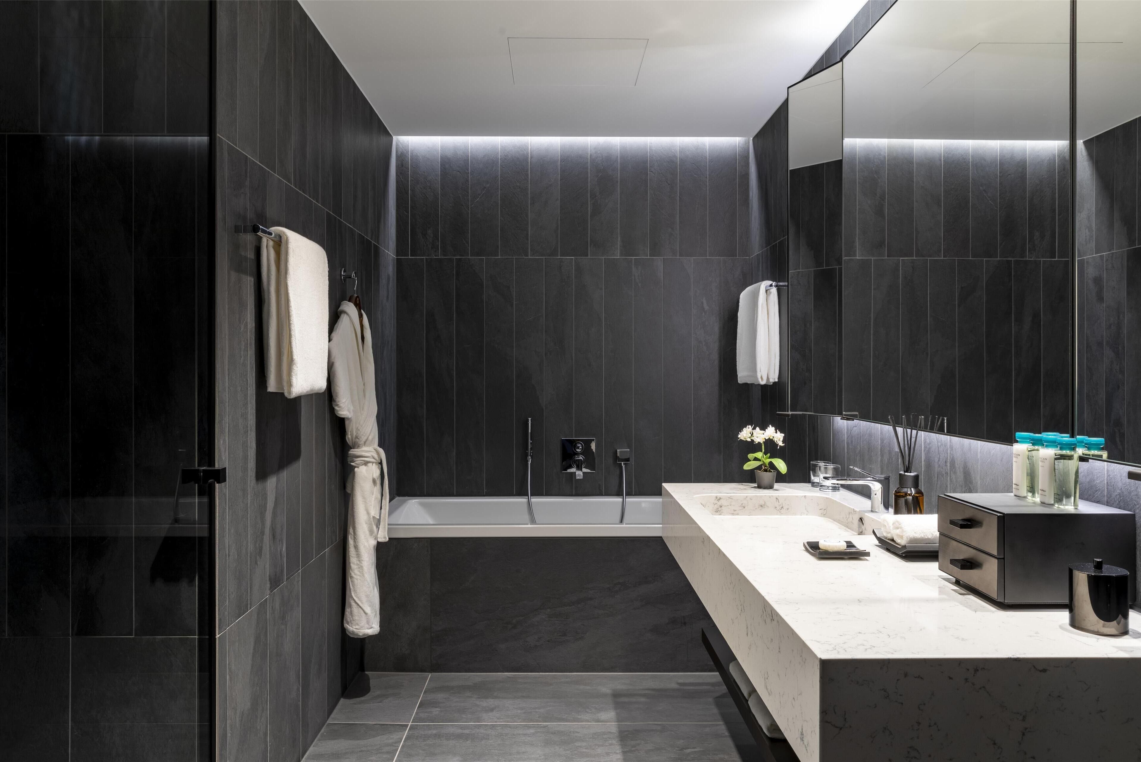 A modern bathroom with dark tiles, a bathtub, a vanity with a mirror, and a towel rack.