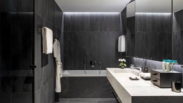 A modern bathroom with dark tiles, a bathtub, a vanity with a mirror, and a towel rack.