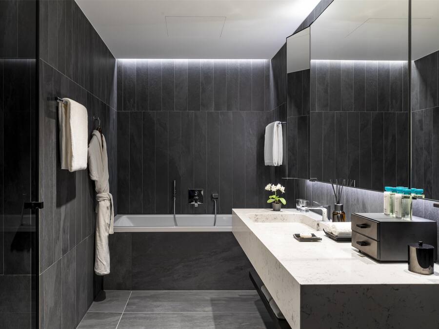 A modern bathroom with dark tiles, a bathtub, a vanity with a mirror, and a towel rack.