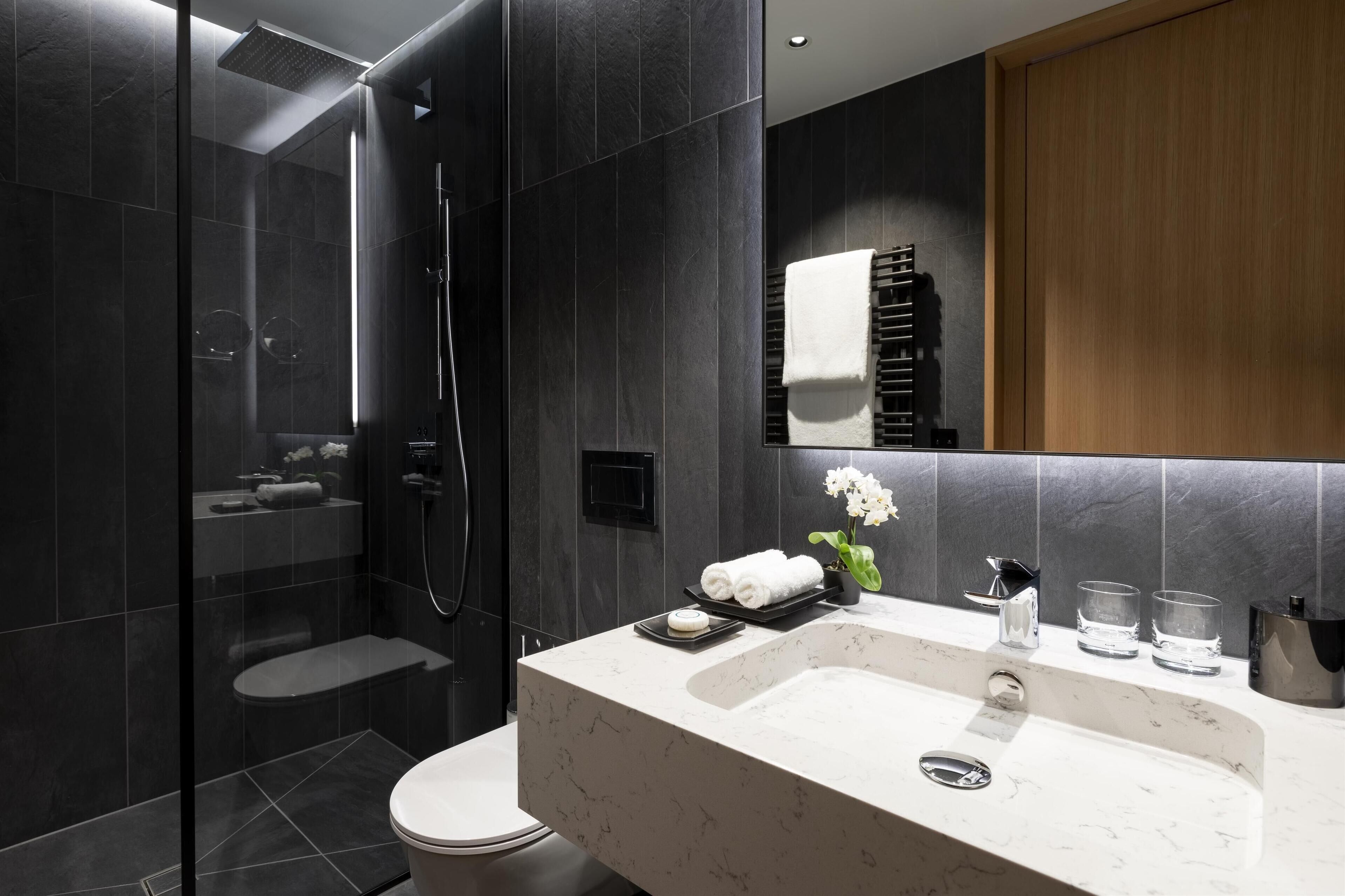 A modern bathroom with a glass-enclosed shower, a marble sink, and a wooden cabinet.