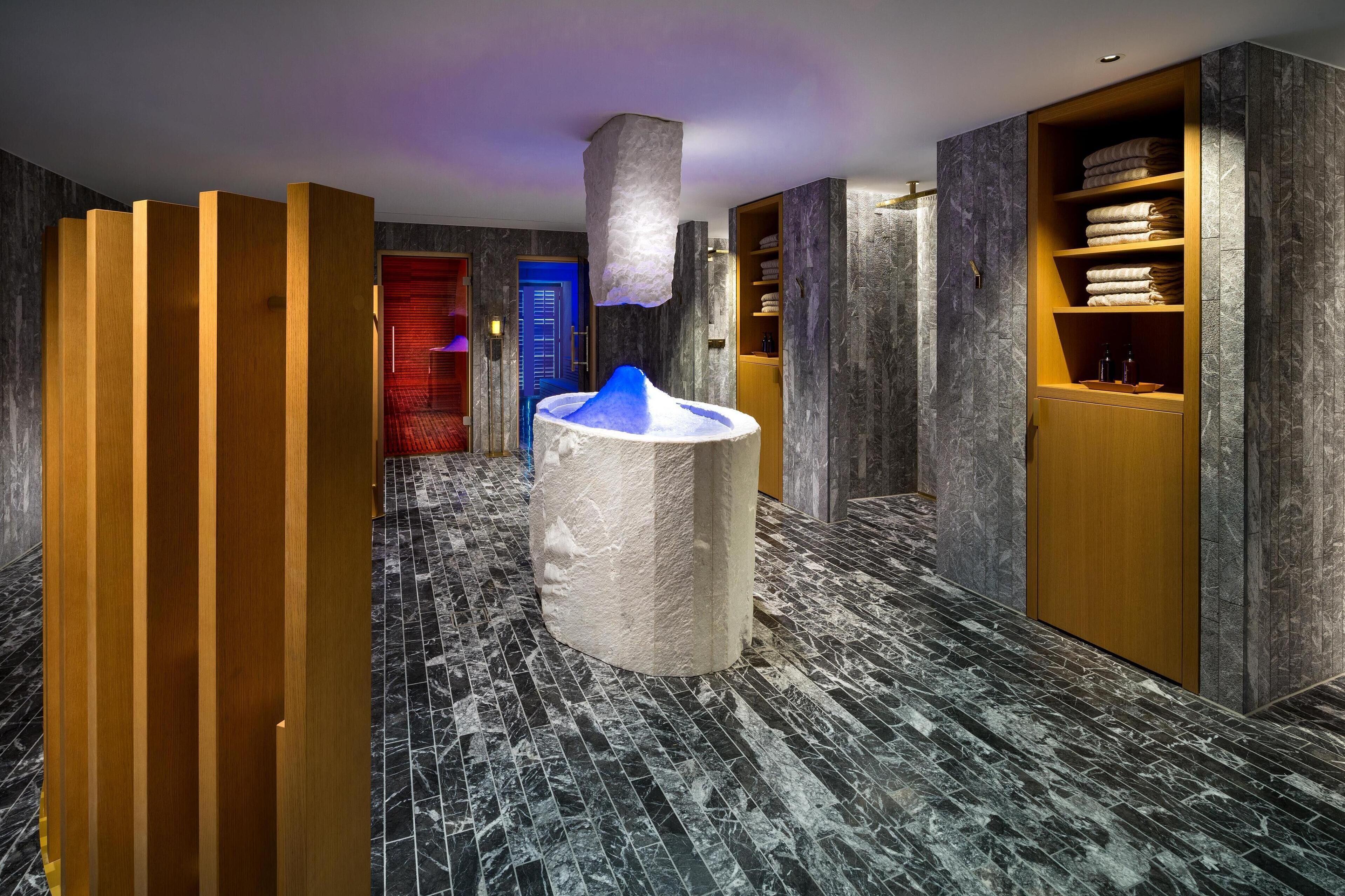 A modern hotel lobby with a marble floor, a central ice sculpture, wooden partitions, and a blue door in the background.