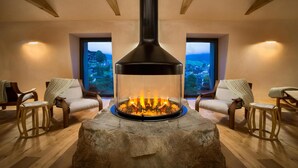 Una habitación acogedora con chimenea de piedra, sillas de madera y vistas a un pueblo a través de amplios ventanales.