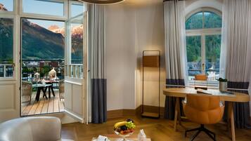 A modern hotel room with a wooden dining table, a comfortable sofa, and a large window offering a scenic mountain view.