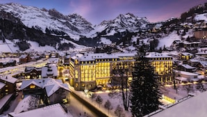 Un pueblo en la montaña cubierto de nieve al anochecer, con un hotel destacado que cuenta con numerosas ventanas iluminadas y un patio central.