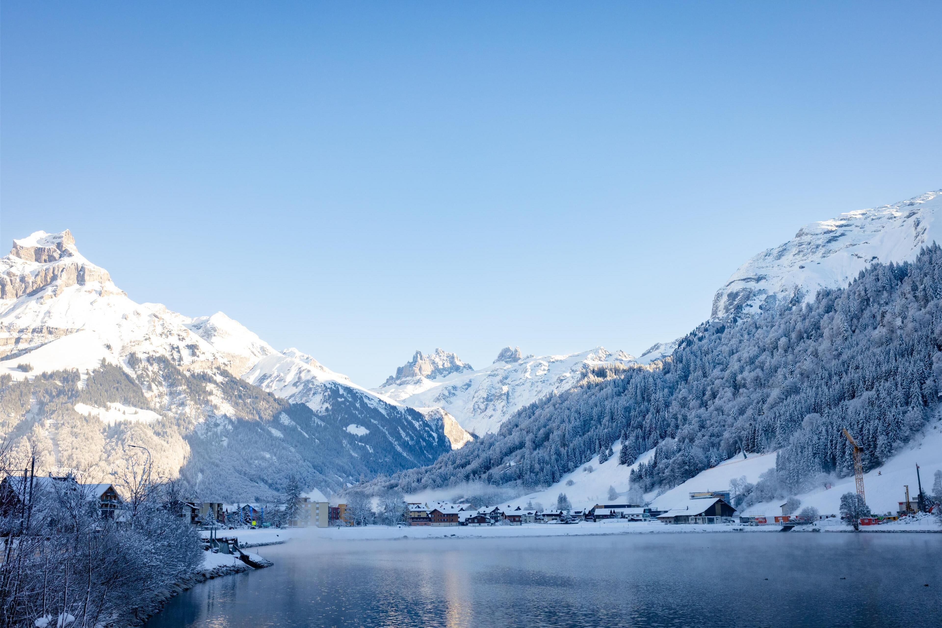Eine verschneite Berglandschaft mit einem See und Gebäuden im Vordergrund.