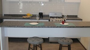 Una cucina moderna con mobili bianchi, un piano di lavoro in granito, due sgabelli da bar e illuminazione a sospensione.