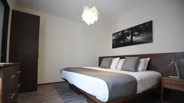 A bedroom with a bed, wooden headboard, bedside tables, a dresser, a hanging light fixture, and a wall-mounted picture.