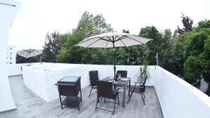 A rooftop terrace with a table and chairs, a large umbrella, and a potted plant.