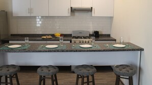 A modern kitchen with white cabinets, a granite countertop, and four bar stools.