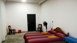 Una habitación con cama, una silla, un ventilador y una mesa.
