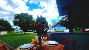Una mesa para comer al aire libre con platos, un jarrón con flores y un vaso de zumo de naranja.