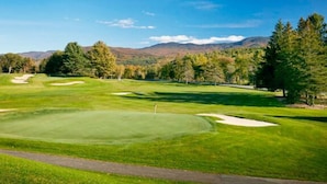 Un campo de golf con un green impecable, búnkeres de arena y un cielo despejado.