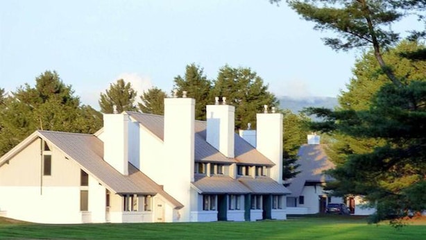 Una casa moderna con varias chimeneas, techo inclinado y césped cuidado.