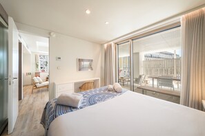 A hotel room with a large bed, a desk, a chair, a balcony with a view, and a window.