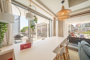 A modern hotel room with a large window, a dining area, and a view of the cityscape.