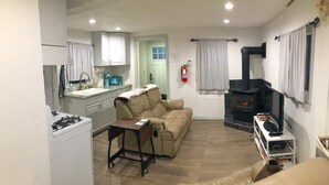A compact living space with a kitchenette, a sofa, a small table, a TV, and a fireplace. - Teakettle Kottage (Columbia Falls)