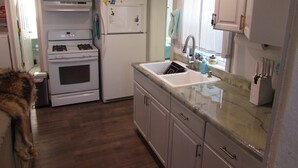A compact kitchen with white cabinets, a built-in oven, a refrigerator, and a sink. - Teakettle Kottage (Columbia Falls)