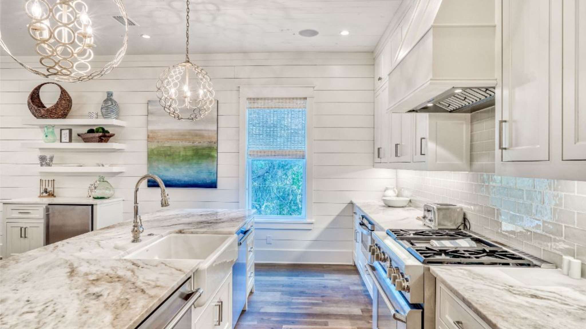 A modern kitchen with white cabinetry, a marble countertop, a built-in stove, and pendant lighting.